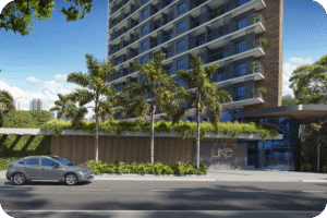 Vista do térreo da torre residencial de alto padrão LIKE Residencial. A imagem destaca a entrada envidraçada com a logo do empreendimento, um painel de madeira na base, abundante vegetação lateral e coqueiros, além de um carro cinza estacionado na rua.